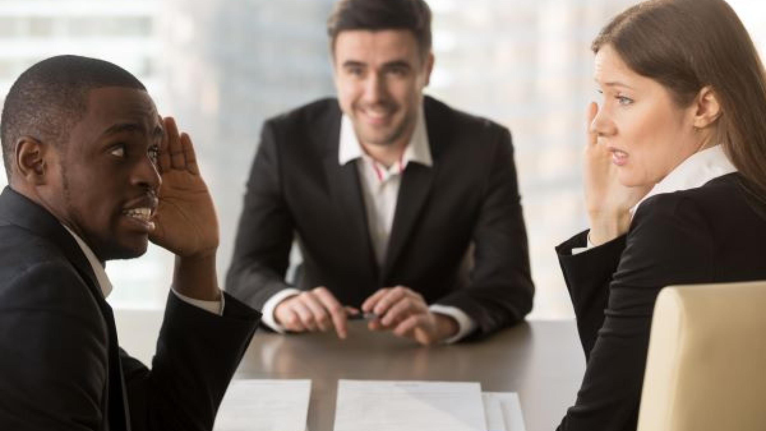 Drie mensen aan bureau, waarvan er twee zich vreemd gedragen. 