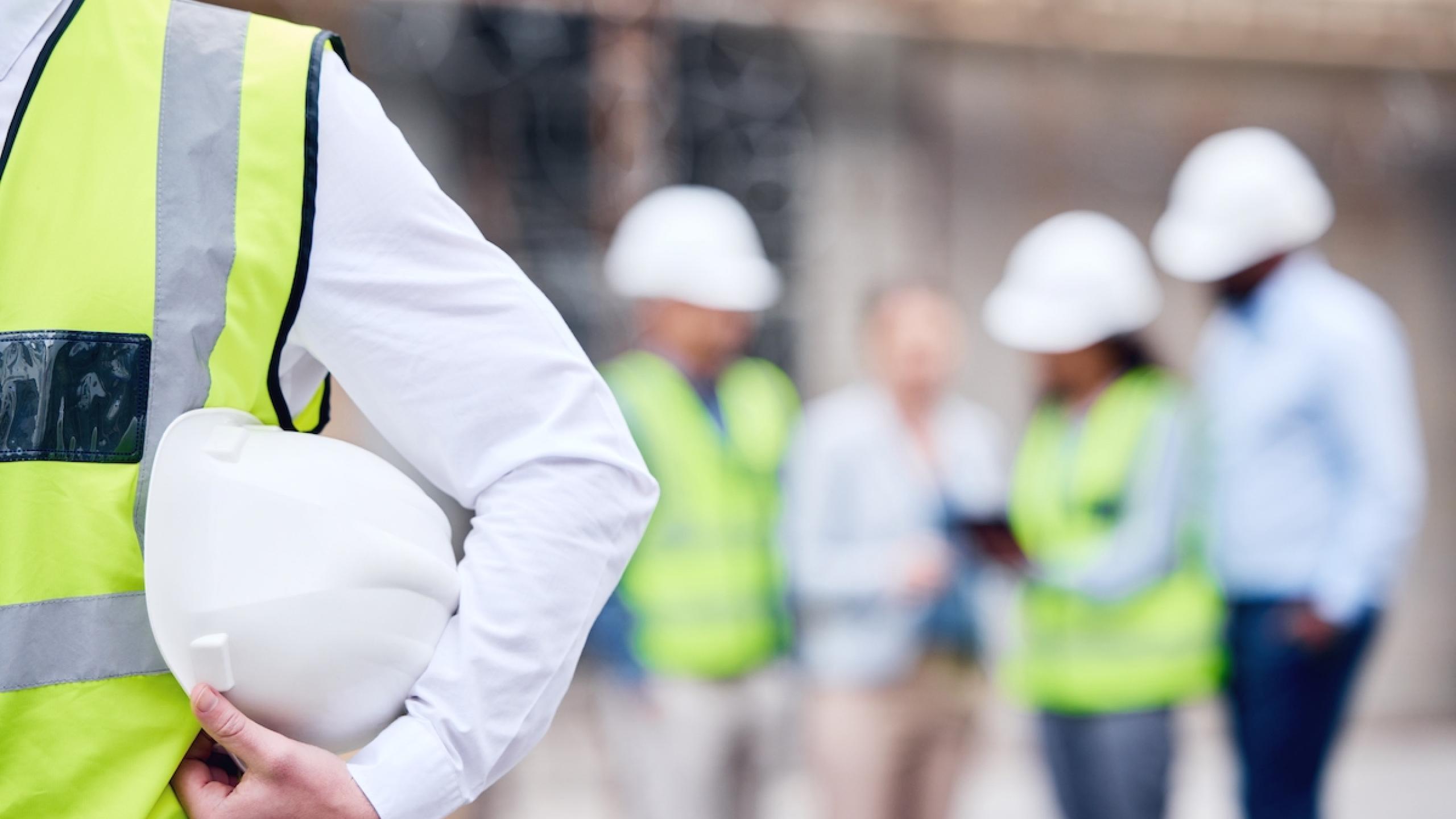 Close-up helm onder de arm en groep professionals op bouwplaats.