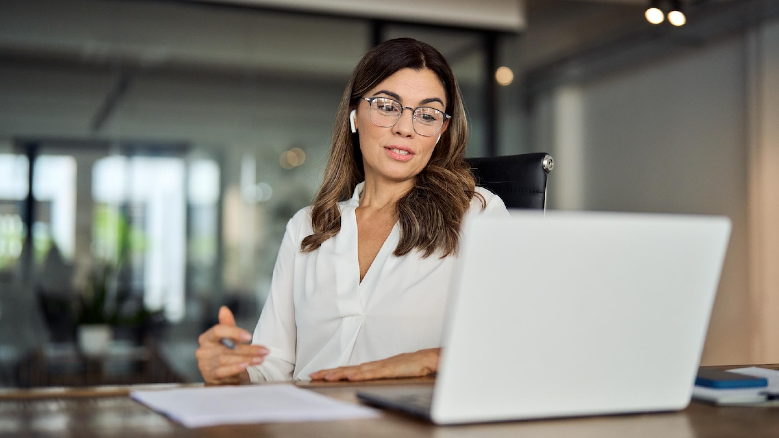 Manager met oortjes in zit aan bureau en kijkt naar computer.