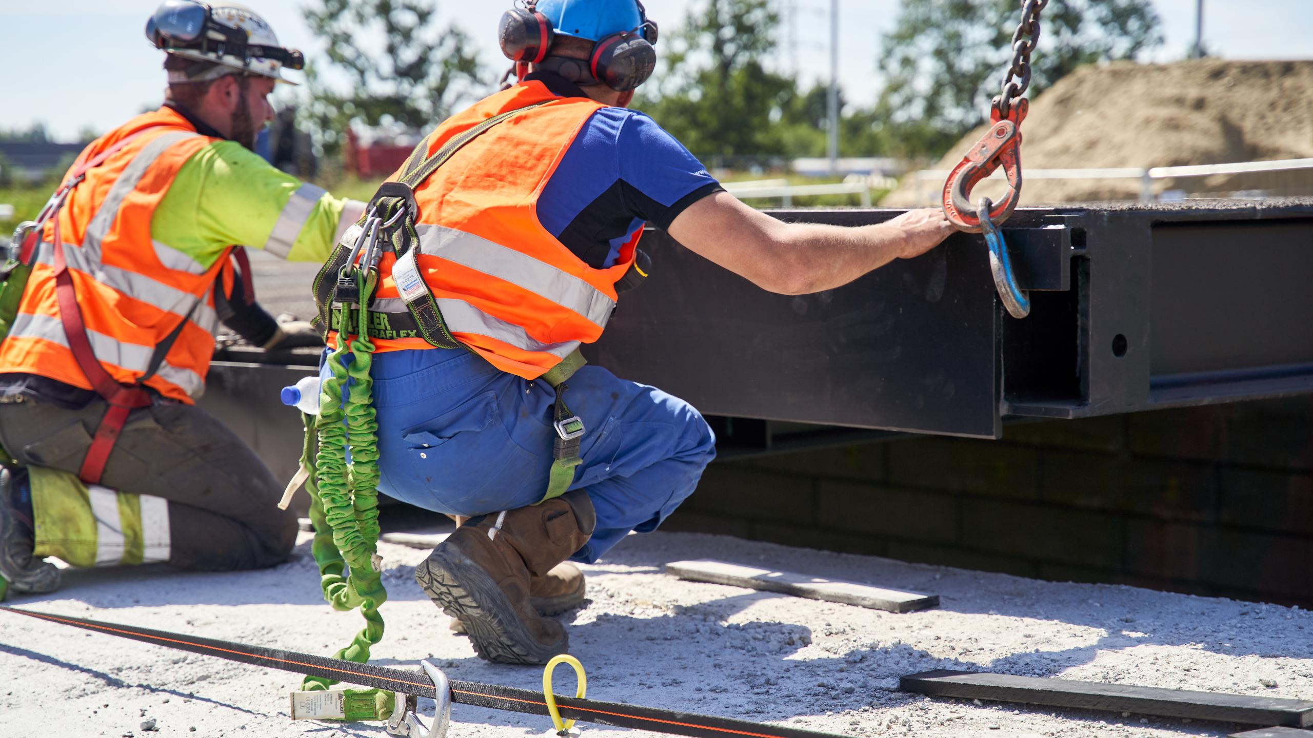 Twee arbeiders met valbescherming bij plaatsing brug.