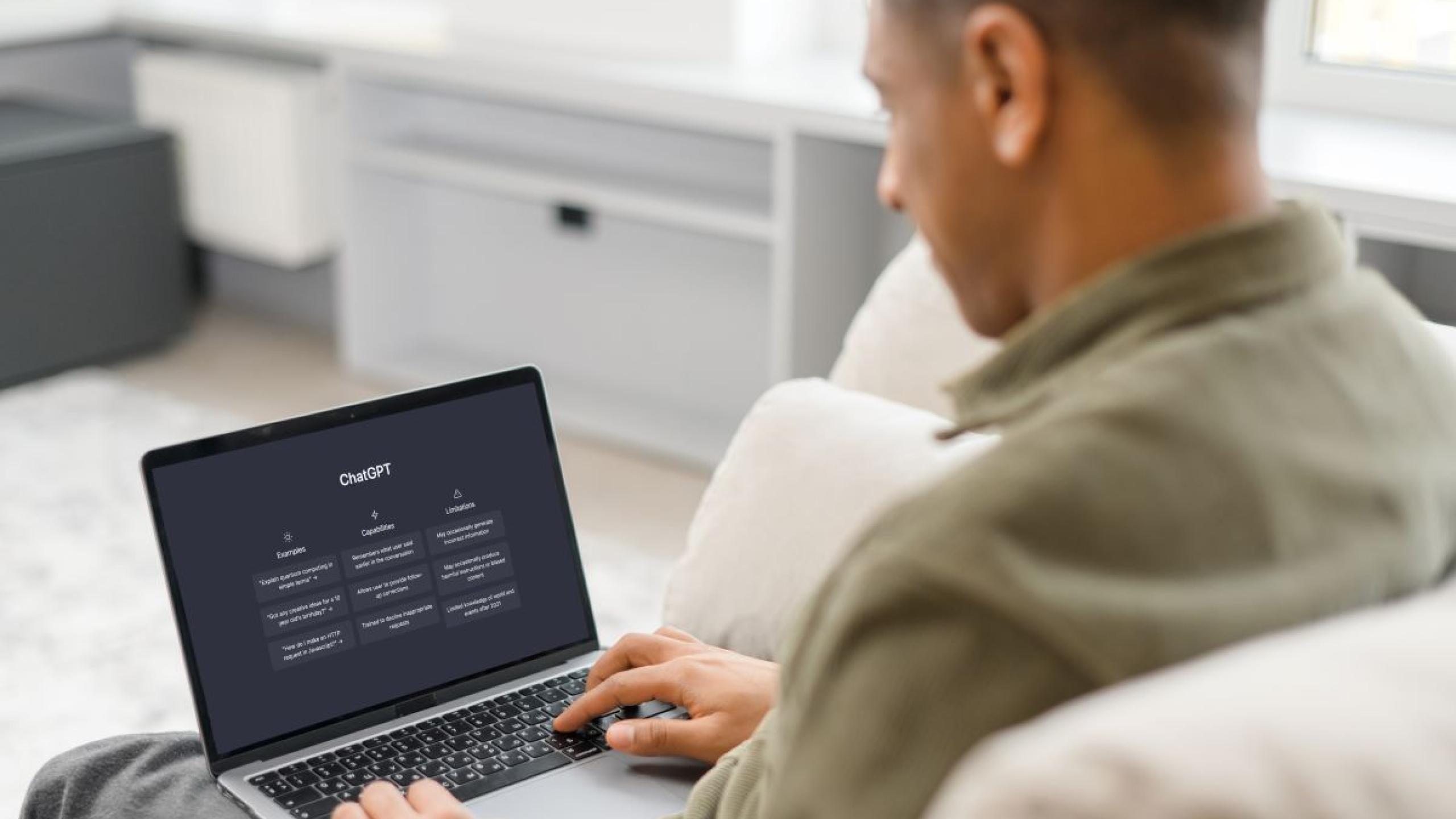 Man in sofa met laptop waarop ChatGPT staat.