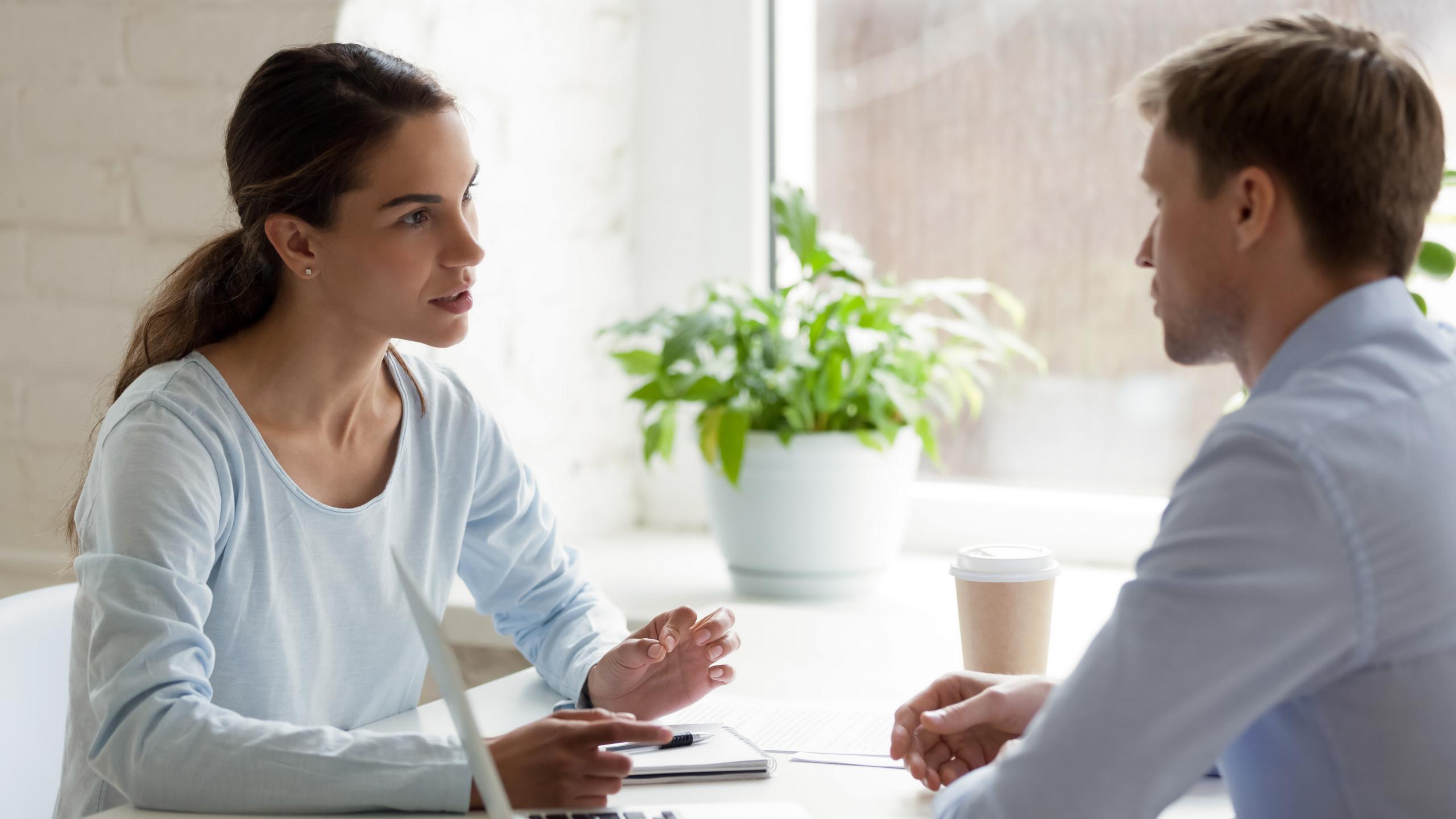 Man en vrouw in gesprek aan bureau.