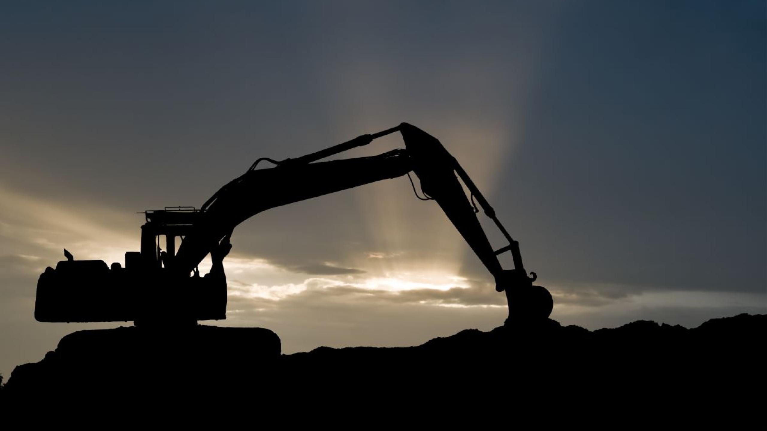 Silhouet van graafmachine met donkere wolken.
