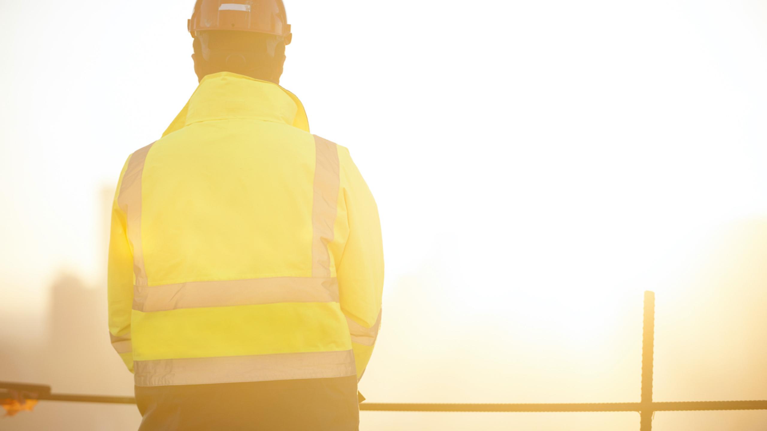 Bouwvakker staat met de rug naar de kijker in de richting van de zon. 