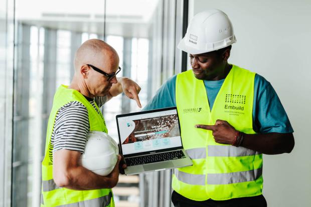 Twee mannen in fluohesjes wijzen naar laptop.
